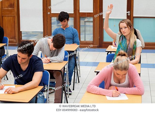 Woman raising hand during exam in exam hall in college