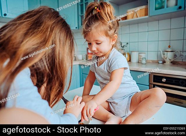 Two little girls in the kitchen sitting on the table. Happy family, happy children