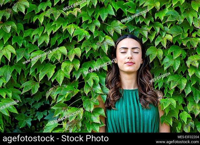 Beautiful young woman with eyes closed leaning on ivy leaves