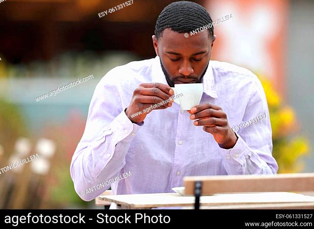 Front view portrait of a man with black skin drinking coffee in a bar terrace