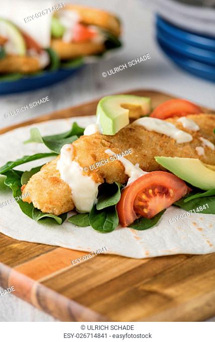 Fish finger wraps with avocado and tomato serves on wooden cheese platter