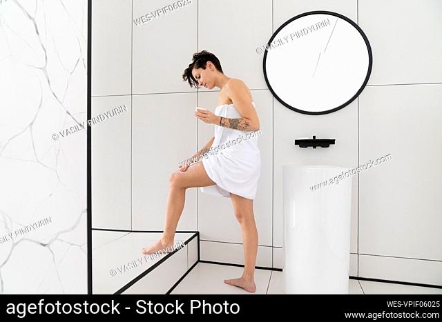 Woman applying moisturizer standing in bathroom at home