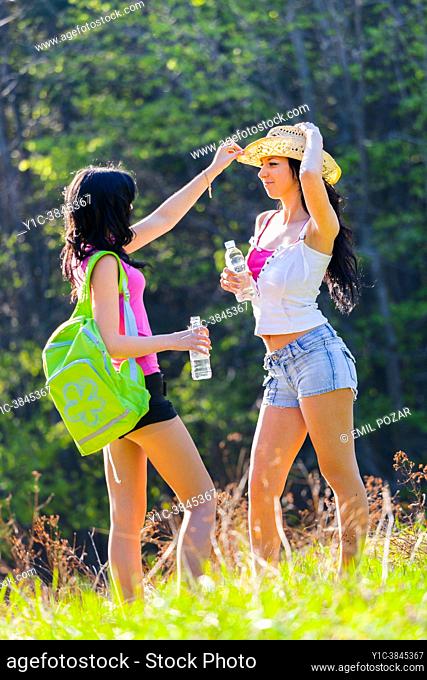 Two adolescent teen girls in nature happy and playful with a straw hat