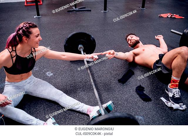 Young woman and man training together, touching fingers over barbell in gym