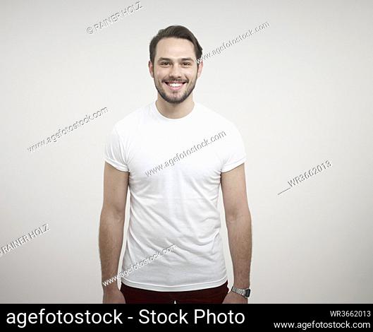 Portrait of young man standing against white background, smiling