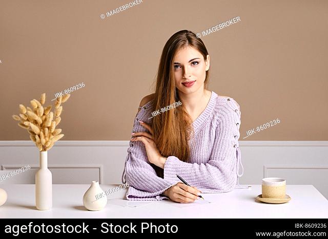 Kind young woman sits behind the table and signs greeting postcard