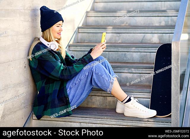 Smiling woman in knit hat using mobile phone on steps