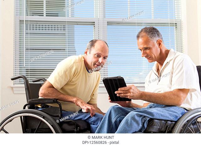 Two disabled men sitting in wheelchairs looking at a digital tablet