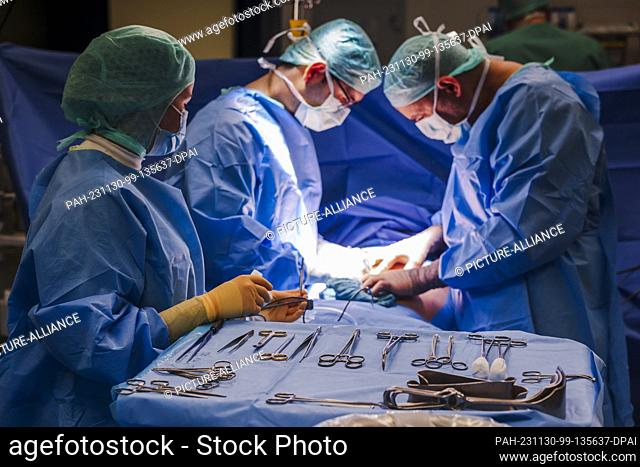 PRODUCTION - 29 November 2023, Schleswig-Holstein, Rendsburg: Doctors and surgical staff stand at the operating table during an operation in the Schön Klinik's...