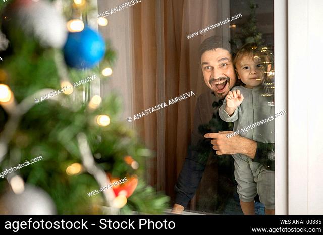 Happy father with son looking at Christmas tree through window