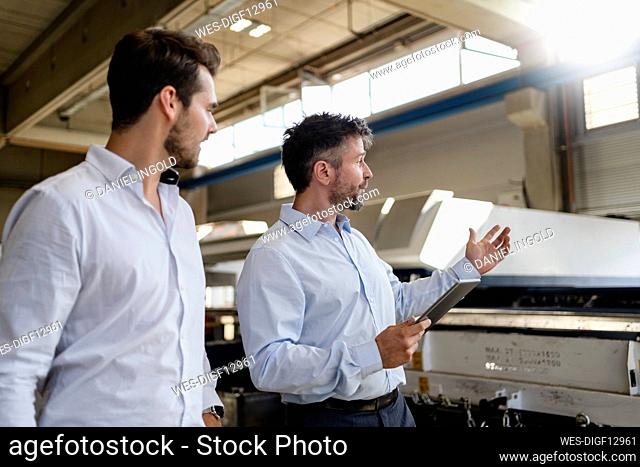 Mature businessman with digital tablet discussing with colleague while standing at factory