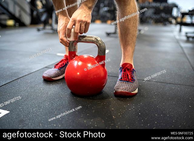 Legs of man holding kettlebell while standing in gym