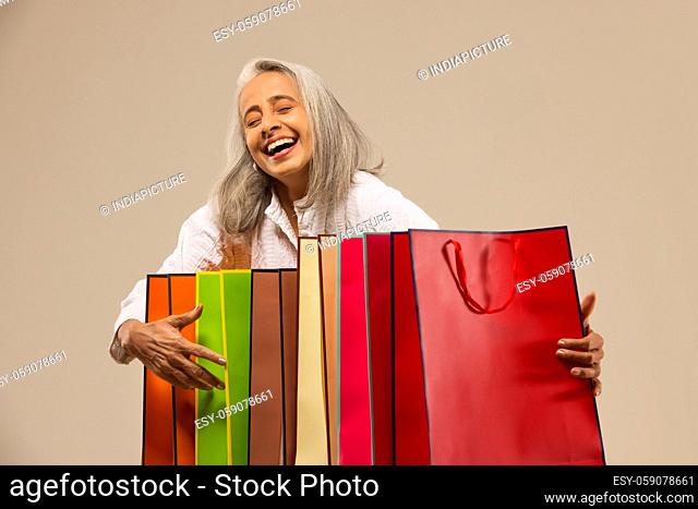 An old woman happily holding colorful carrybags