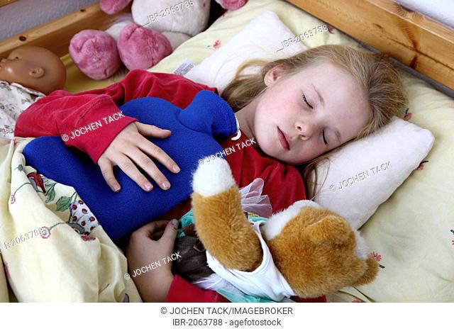 Girl, 10 years old, is ill in bed with a cold, flu, fever, holding a hot-water bottle