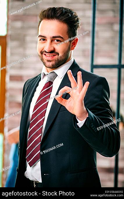 Attractive Bearded Man In A Suit Shows Ok Sign. Portrait Of Smiling Businessman Gesturing An Ok Sign