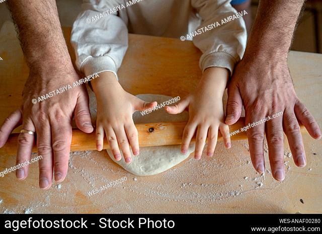 Hands of son and father rolling pizza dough in kitchen