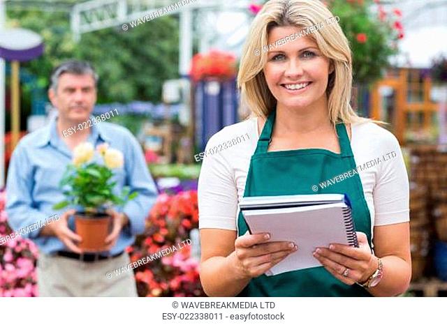 Smiling woman holding notepad with doing holding plant in background in garden c