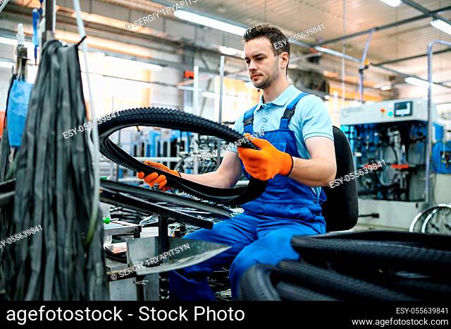 Worker at the assemly line holds bicycle tire on factory. Bike wheels production in workshop, cycle parts installation, modern technology