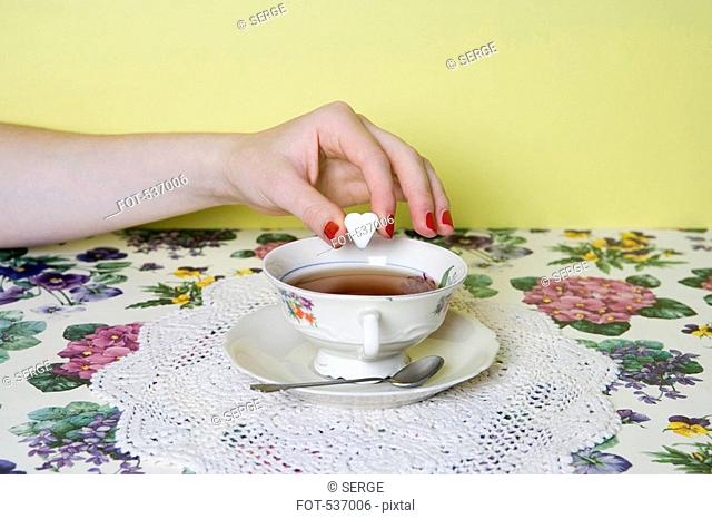 A woman's hand dropping a heart shaped sugar cube into a cup of tea