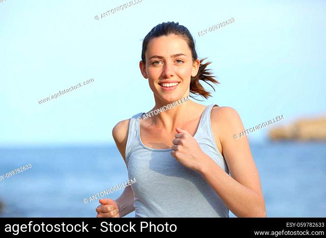 Front view of a happy runner running towards camera on the beach