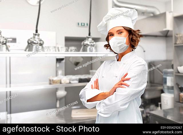 female chef in mask with crossed arms at kitchen
