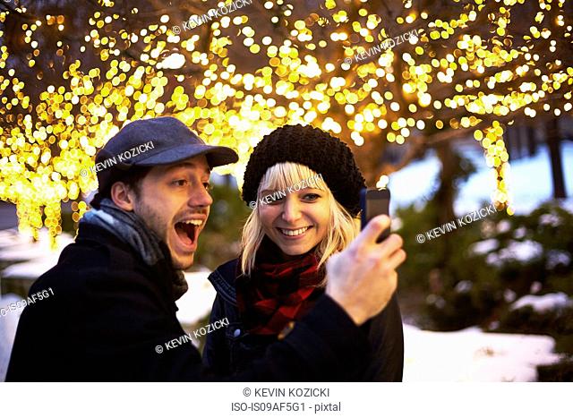 Young couple taking self portrait with outdoor xmas lights