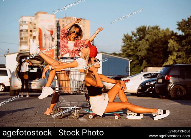 Young women with a supermarket cart have fun in the car park