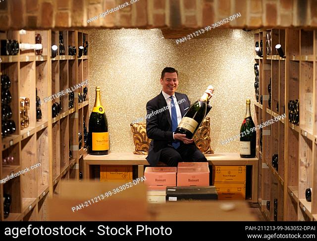 30 November 2021, Hamburg: Ingo C. Peters, director of Hamburg's luxury hotel Vier Jahreszeiten, sits in the hotel's wine cellar holding a bottle of champagne