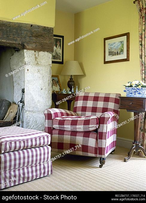 Country cottage sitting room detail with a chequered armchair and ottoman next to an inglenook fireplace