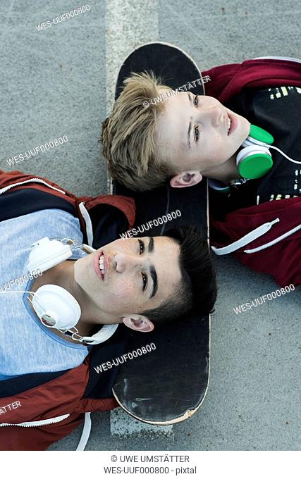 Two boys wearing headphones lying on ground