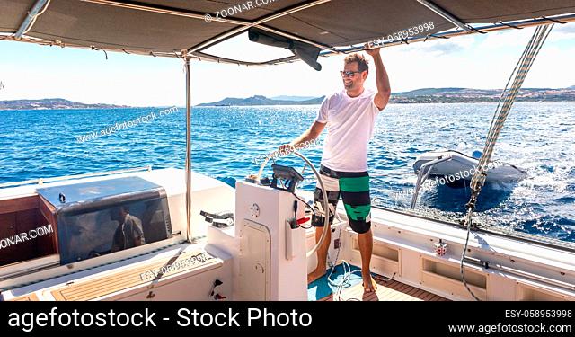 Attractive male skipper navigating the fancy catamaran sailboat on sunny summer day on calm blue sea water. Luxury summer adventure, active nautical vacation
