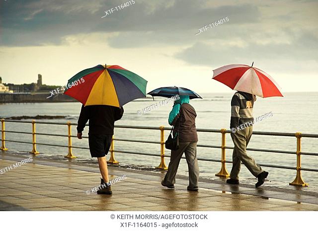 Three people sheltering under umbrellas on a wet summer evening, Aberystwyth Wales UK