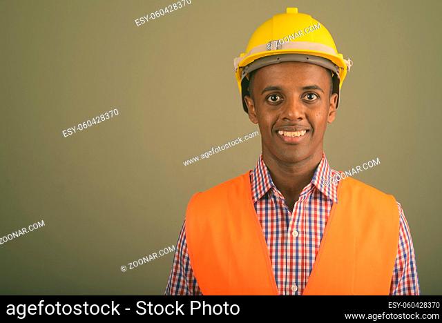 Studio shot of young handsome African man construction worker against colored background