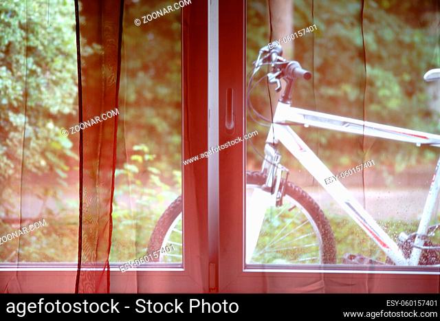 Ein Mountainbike Fahrrad steht hinter den Gardinen eines Fensters