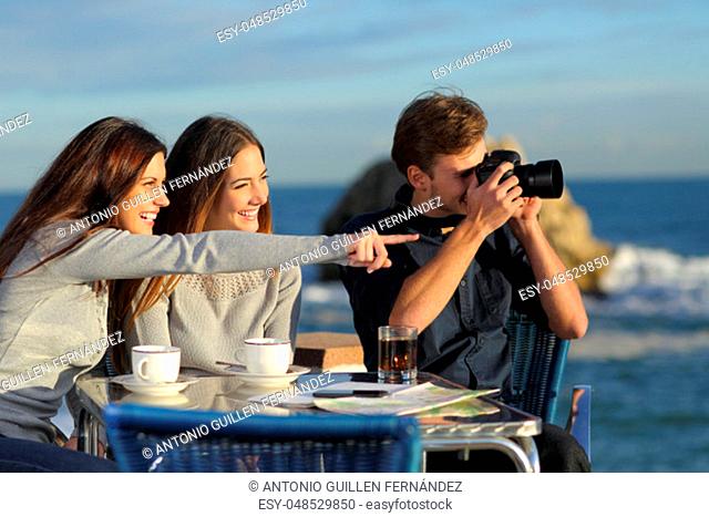 Three happy tourists taking photos from a coffee shop on the beach on vacation