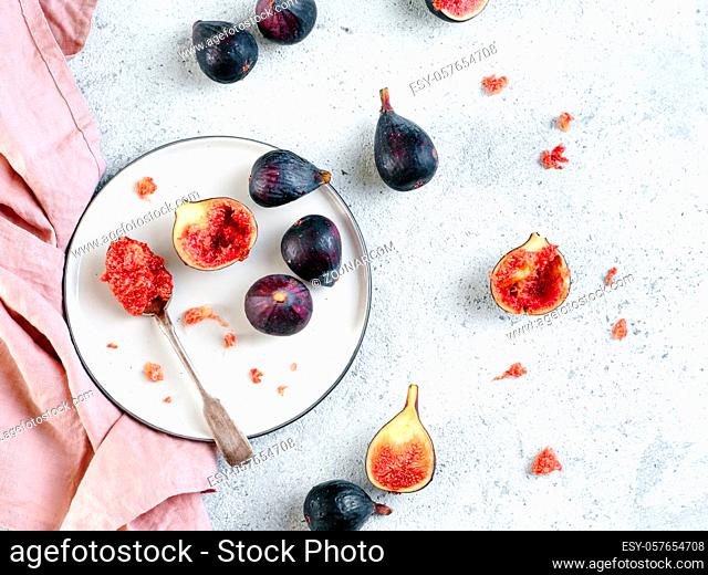 Half and whole figs on gray cement or stone background. Figs flesh in teaspoon on plate and figs on tabletop. Top view or flat lay. Horizontal