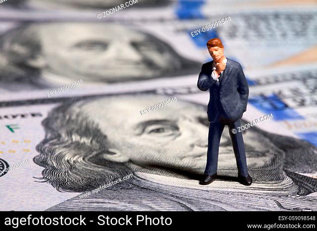 Miniature figurine businessman with 100 dollars banknote on background. Concept