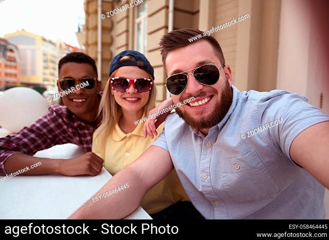 Picture of happy friends posing for camera. Happy peole making selfies on mobile or smart phone outdoors. People spending free time in city centre
