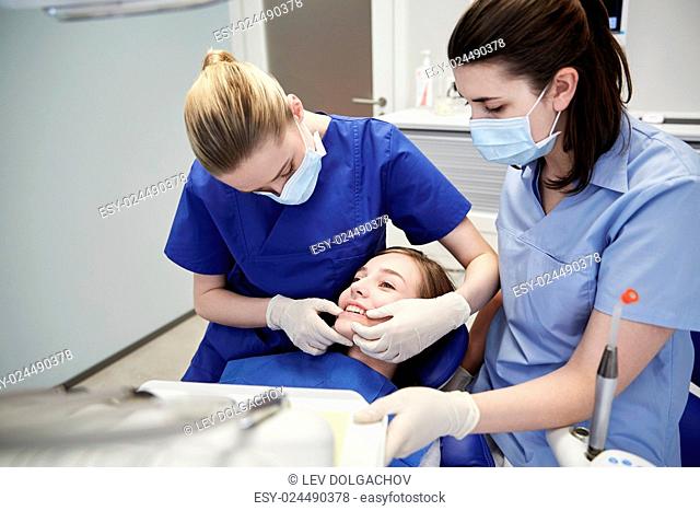 people, medicine, stomatology and teeth care concept - happy female dentist with assistant checking patient girl dental occlusion teeth at dental clinic office