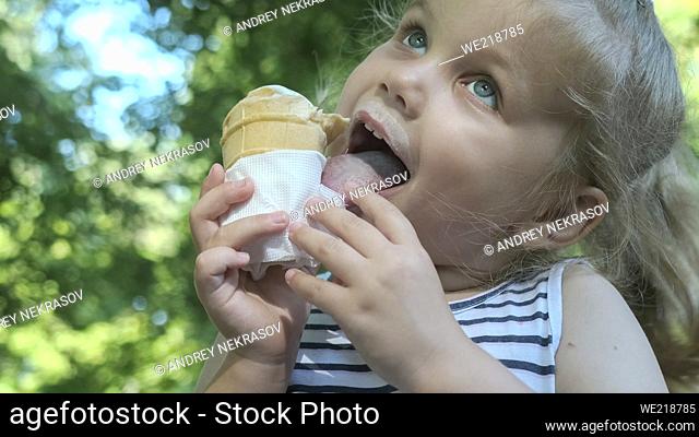 Cute little girl eats ice cream outside. Close-up portrait of blonde girl sitting on park bench and eating icecream