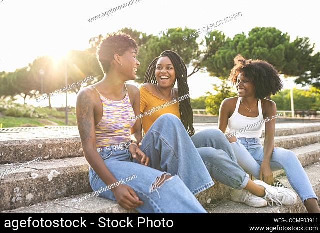 Cheerful female friends laughing sitting on steps in park