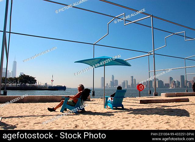 03 October 2023, USA, New York: People sitting on Manhattan's first beach, the Gansevoort Peninsula. At the end of summer, of all times