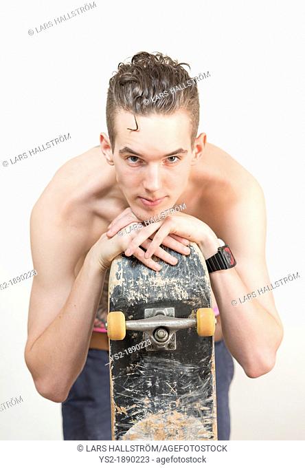 Confident and cool young adult man holding a skateboard and looking at camera