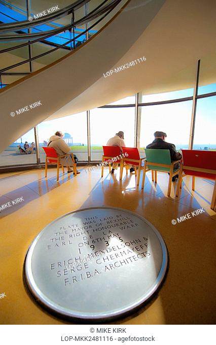 A plaque commemorating the opening of the De La Warr Pavilion in 1935 and people relaxing inside enjoying the view of the sea