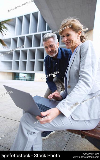 Businesswoman sharing laptop with businessman sitting on bench