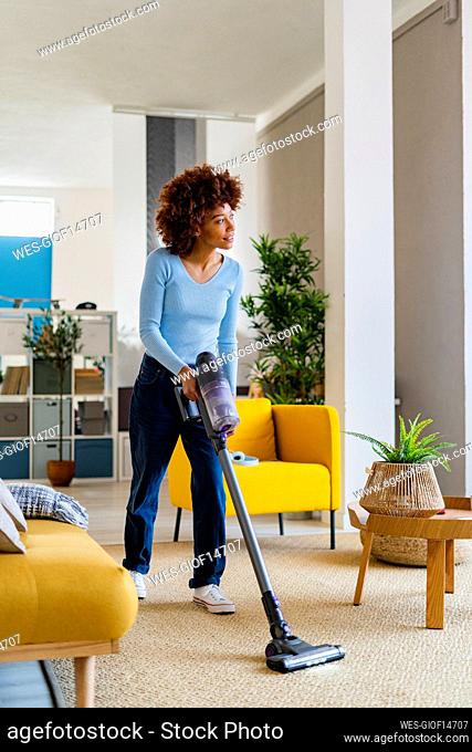 Young Afro woman cleaning carpet in living room at home