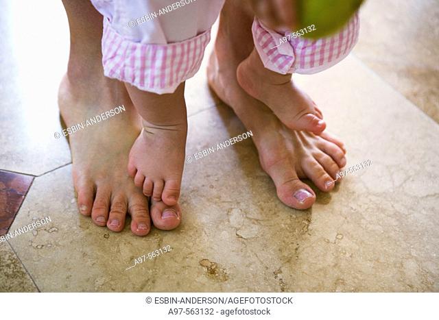 Close-up of mother and infant girl's barefeet. Infant is standing on mother's feet