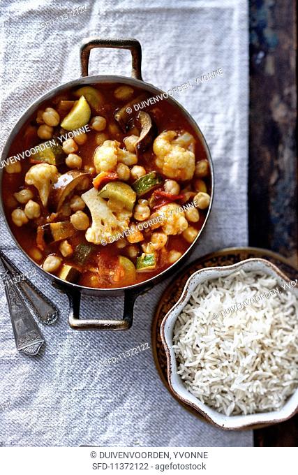 Vegetable curry with chickpeas, aubergines, courgettes, cauliflower and tomato in a pot served with a bowl of jasmine rice