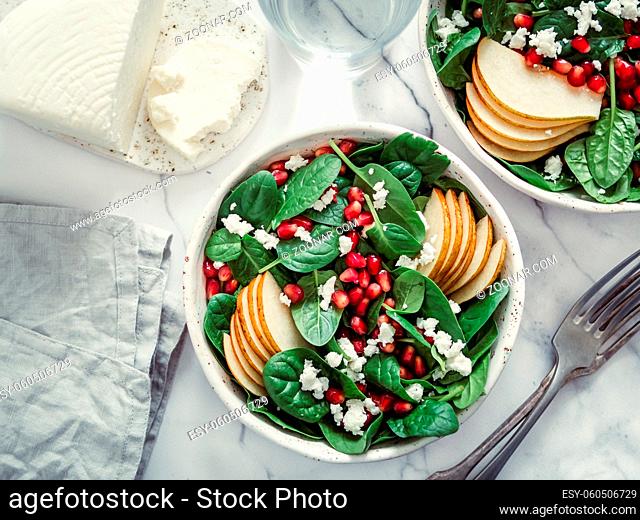 Fresh salad with baby spinach, pear, pomegranate and cottage cheese. Two bowls with delicious summer fruit salad on marble table. Copy space for text