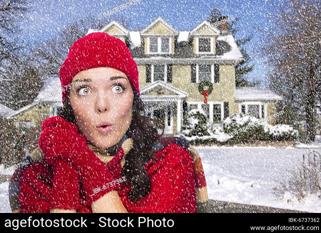 Smiling mixed race woman looking to the side in winter clothing outside of decorated house in the falling snow